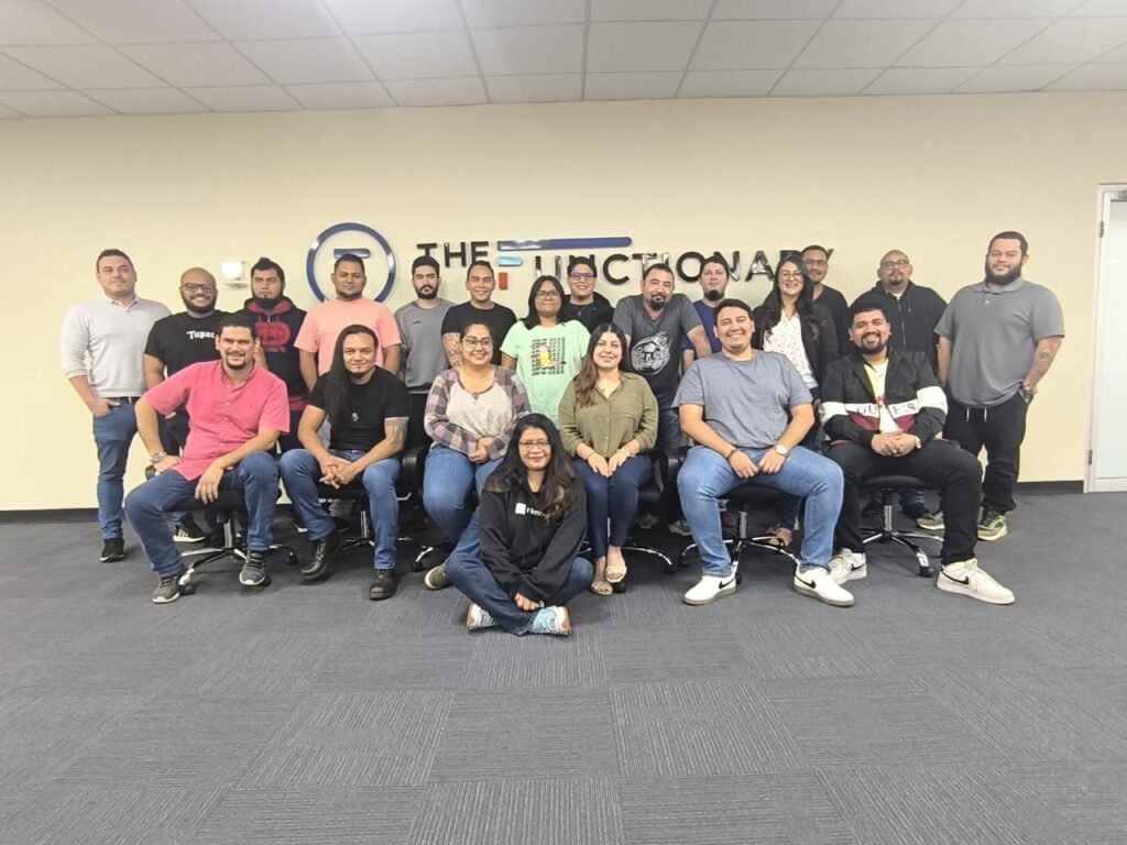 Photo of a group of 30 people posing in front of a company logo in their office space.