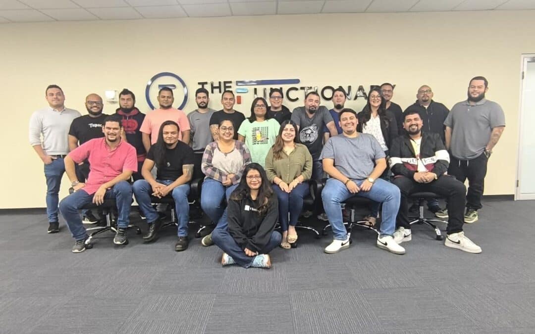 Photo of a group of 30 people posing in front of a company logo in their office space.
